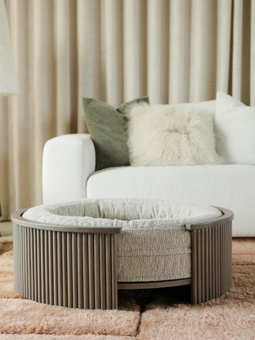 Fantail Elite grey oak dog bed frame in a living room with a cushion, complementing modern decor.