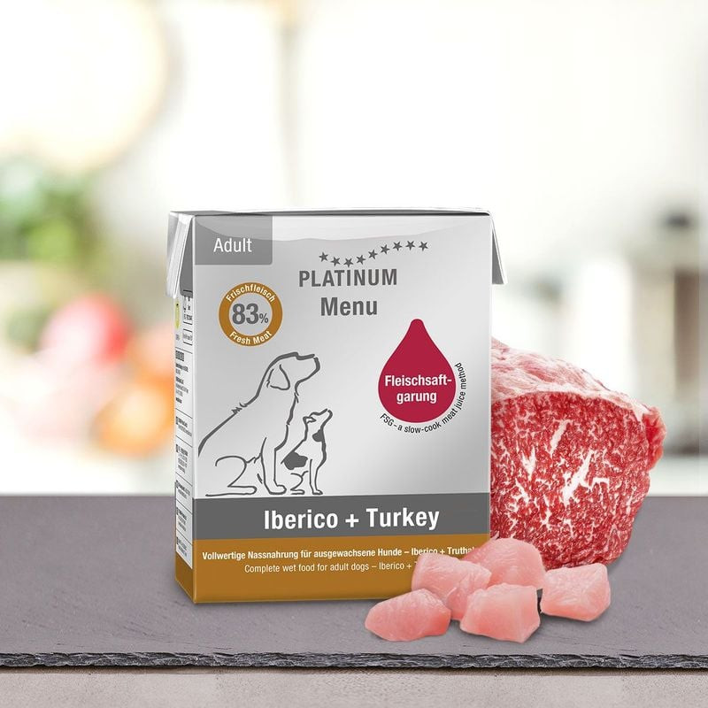 Pâtée PLATINUM Iberico + Dinde pour chien sur table de cuisine avec steak de porc ibérique cru frais