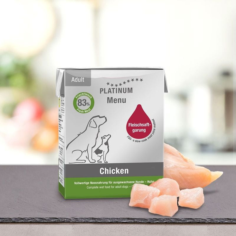 Emballage PLATINUM Menu Adulte Poulet pour chien sur table avec morceaux de poulet frais à proximité