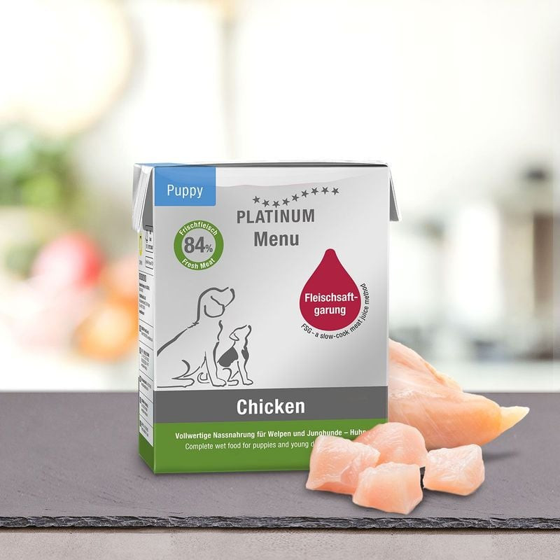 Vue ambiante du carton Platinum Puppy Menu Poulet près de morceaux de poulet cru frais sur ardoise a