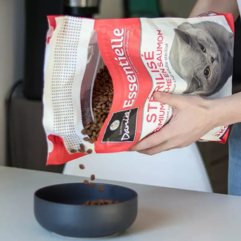 Scène lifestyle : main versant croquettes saumon Les Recettes de Daniel du sac 3kg dans bol noir, pe