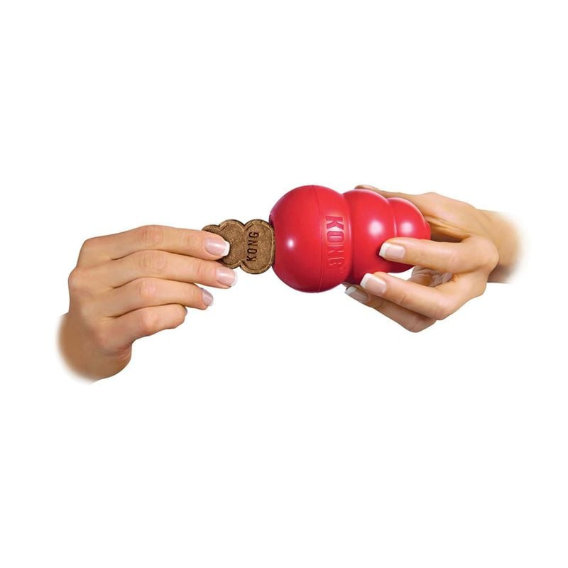 Mains démontrant l'insertion d'une friandise foie en forme KONG dans un jouet KONG rouge sur fond bl